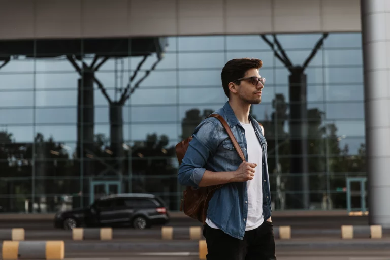 Handsome brunette man denim jacket white t shirt black pants poses outside copy
